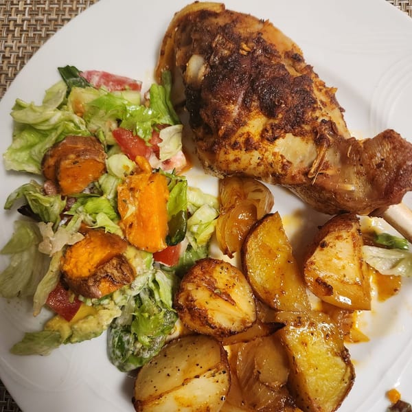 A plate of Mr Nosh's roasted chicken with potatoes, onions, and a fresh salad.
