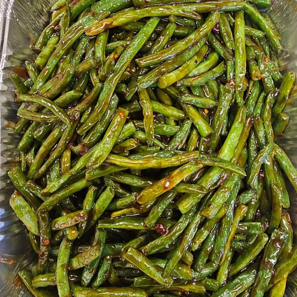 Close-up of glistening green beans, likely stir-fried, in a metal container at Mr Nosh.