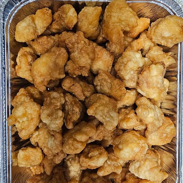 Golden-brown fried chicken pieces, likely General Tso's or orange chicken, in a foil takeout container.