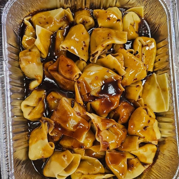 Mr Nosh's Chinese dumplings, glistening with dark sauce and chili flakes, in a foil container.