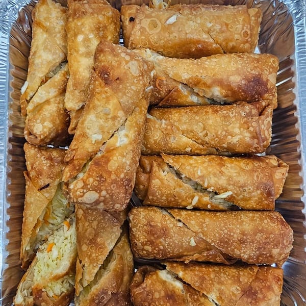 Crispy golden-brown egg rolls, some cut open to reveal a savory vegetable and meat filling, in a foil tray.