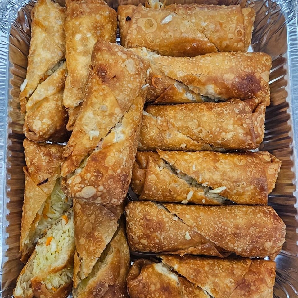 Crispy golden-brown egg rolls, some cut open to reveal a savory vegetable and meat filling, in a foil tray.